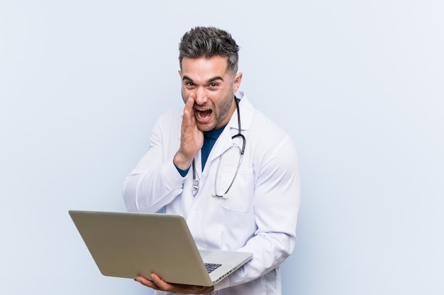 Caucasian doctor man holding a laptop shouting excited to front.