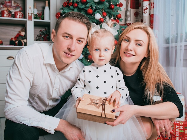 caucasian family father mother and little daughter in christmas sweaters by the christmas tree