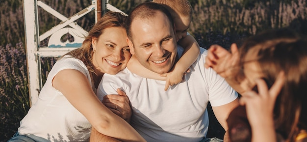 Famiglia caucasica che si siede in un campo di lavanda sorridendo e abbracciando in una giornata di sole