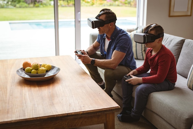 Фото Кавказский отец и сын в гарнитурах виртуальной реальности играют в видеоигры, сидя дома на диване