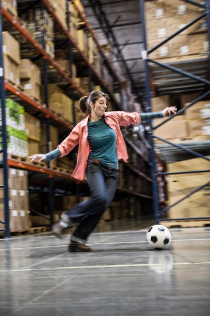 A caucasian female aboiut to kick a soccer ball during a work break in a distribution warehouse