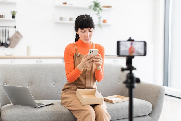 Caucasian female blogger unboxing smartphone in modern living room