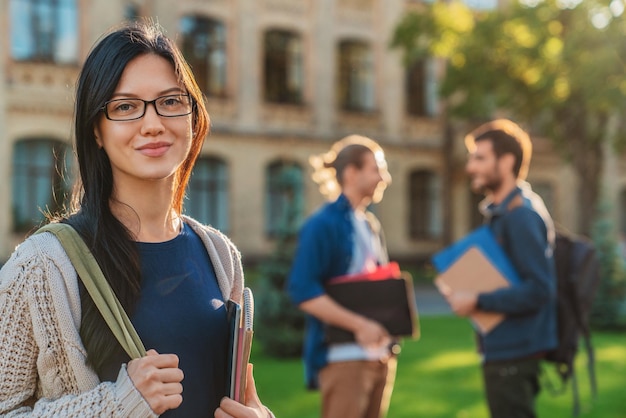 Caucasian female college student on modern campus with friends on background