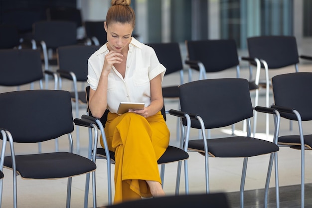 Caucasian female executive looking at digital tablet while sitting on chair in empty conference room