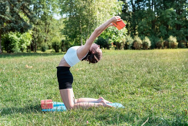 Caucasian female fitness trainer practicing yoga or pilates on green grass in beautiful summer day