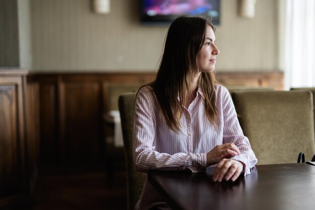 Caucasian female is looks away while sitting at the table in the cafe