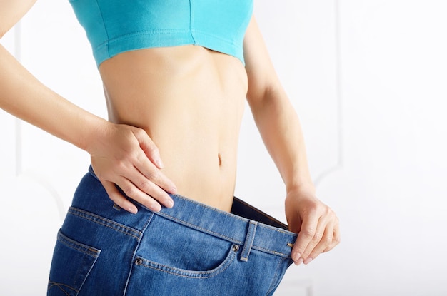 Caucasian female model in blue jeans showing her flat stomach. Weightloss concept.