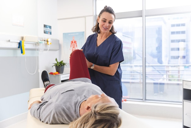 Photo caucasian female physiotherapist and senior woman with artificial leg stretching at hospital