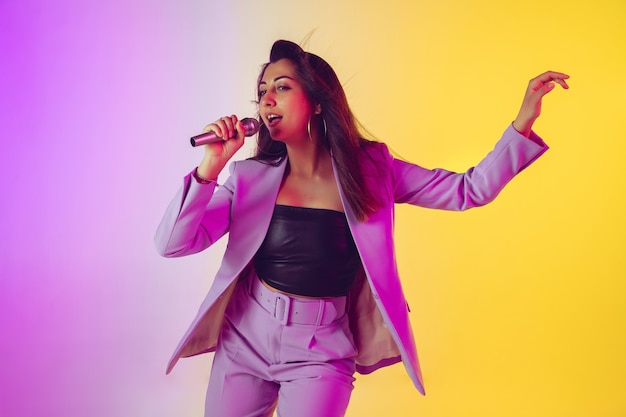 Caucasian female singer portrait isolated on gradient studio background in neon light