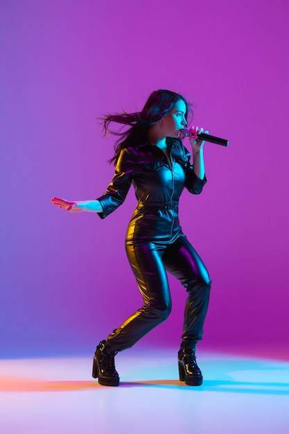 Caucasian female singer portrait isolated on purple studio background in neon light