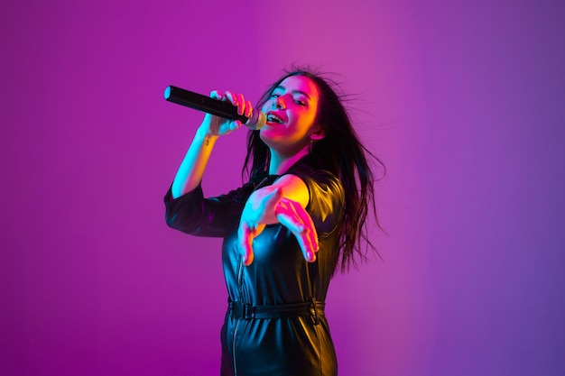 Caucasian female singer portrait isolated on purple studio background in neon light