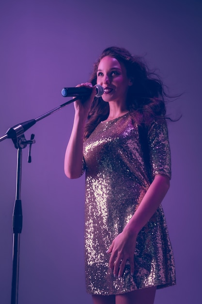 Caucasian female singer portrait isolated on purple studio background in neon light