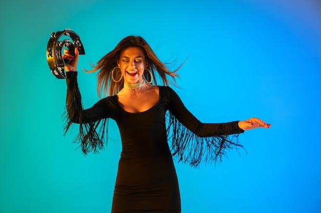 Caucasian female singer with tambourin isolated on blue studio background in neon light