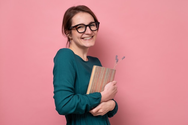 Caucasian female student or teacher in glasses smiling, holding books and looking at camera. Studio shot