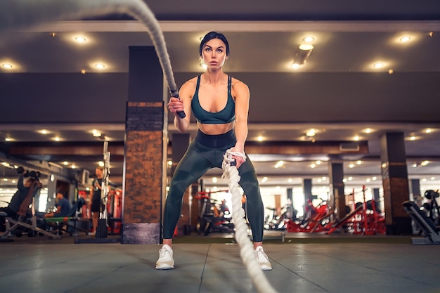 Caucasian fit woman dressed in sportsoutfit posing with battle ropes at gym