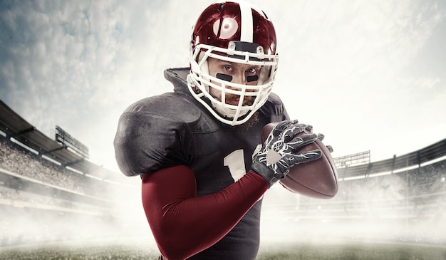 Caucasian fitness man as american football player holding a ball on stadium surface