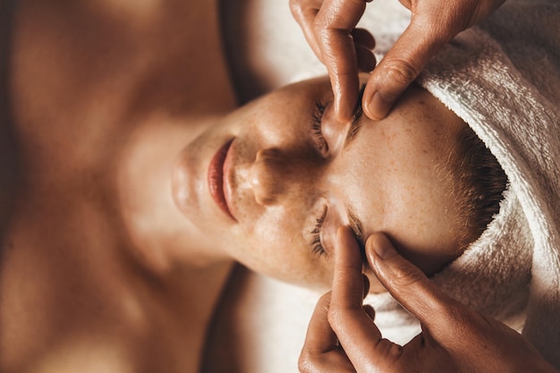 Caucasian freckled woman enjoying facial massage with closed eyes in spa salon Beauty spa healthy lifestyle Facial massage at home Massage the skin around the eyes Wrinkle smoothing