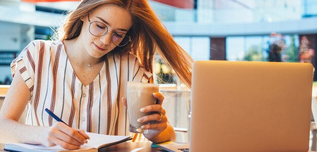 Caucasian ginger entrepreneur having a coffee break from computer work and making some notes