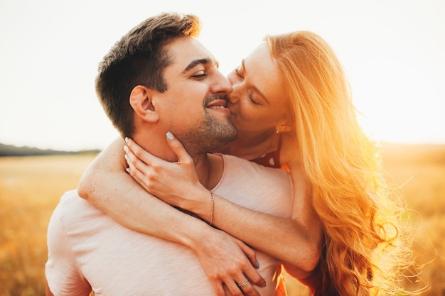 Caucasian ginger lady is embracing her lover kissing him and smile during a sunset in the field