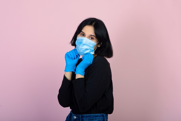 The caucasian girl in blue colored protective face mask. The girl looking at camera. Portrait shot over pink wall. virus and pollution protection concept.