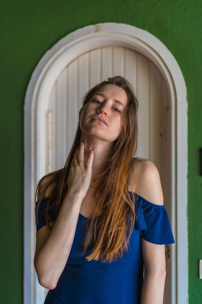 Caucasian girl in a blue dress next to a white door of a green house vertical photo