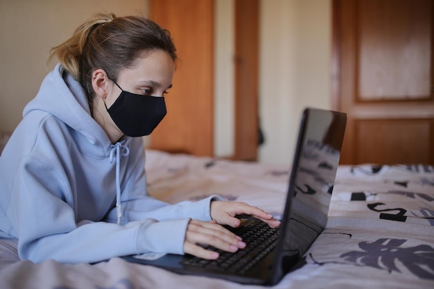 파란색 까마귀와 검은색 마스크를 쓴 백인 소녀는 집에서 격리된 노트북에서 일한다