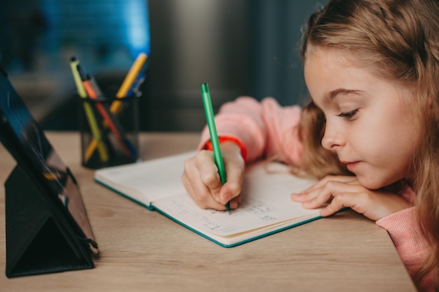 Ragazza caucasica che fa i compiti e studia online con il tablet alla scrivania bambino che studia da casa a casa