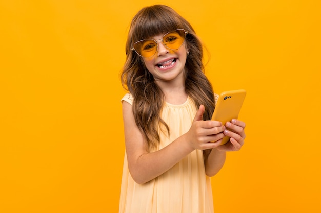 Кавказская девушка в очках с телефоном в руках на желтой стене