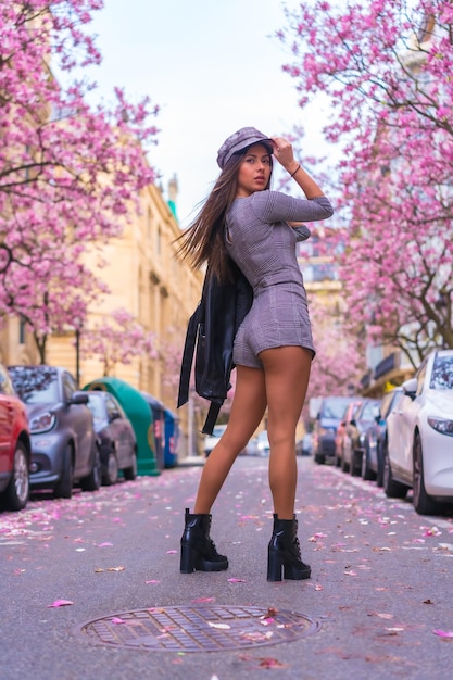 Кавказская девушка в кожаной куртке и берете в городе с цветущими деревьями весной