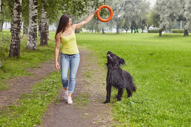 Caucasian girl is using toy to train black briard jumping while they are walking.