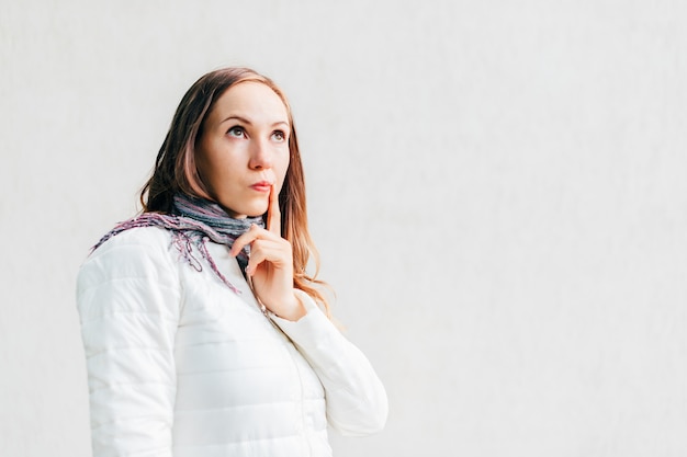 Caucasian girl looks away thoughtfully putting finger to the corner of her mouth.