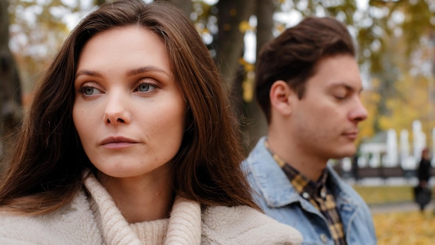 Caucasian girl offended by male lover on background young family couple standing outdoors ignoring