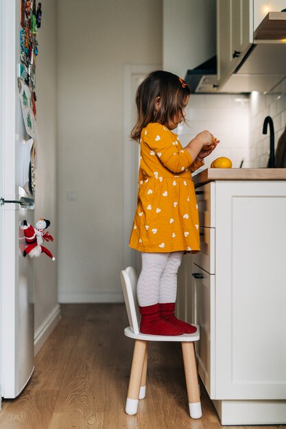 Caucasian girl peeling tangerines on kitchen counter.