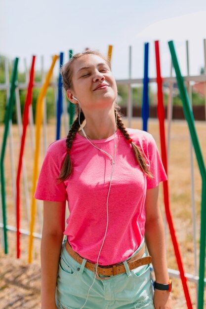 Caucasian girl in a pink T-shirt and white headphones listens to music. Girl student smiles, exposing her face to the sun's rays.