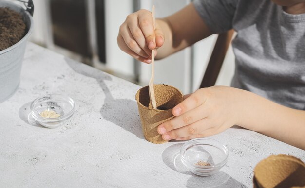 A caucasian girl plants seeds in a cardboard cup picking up the ground