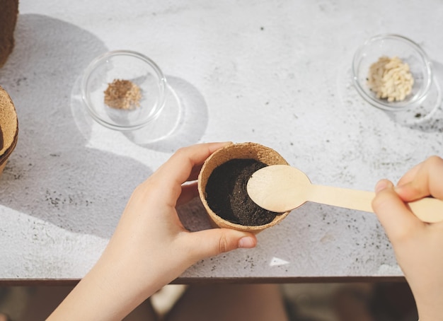 A caucasian girl plants seeds in a cardboard cup picking up the ground