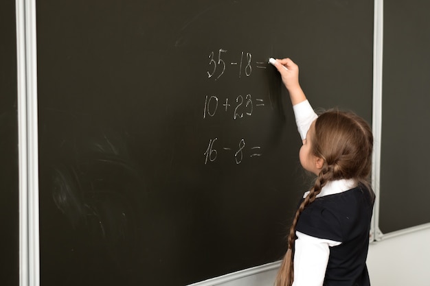 Caucasian girl pupil in front of blackboard solving math task at school