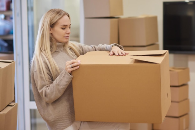 Caucasian girl taping boxes for moving in new apartment