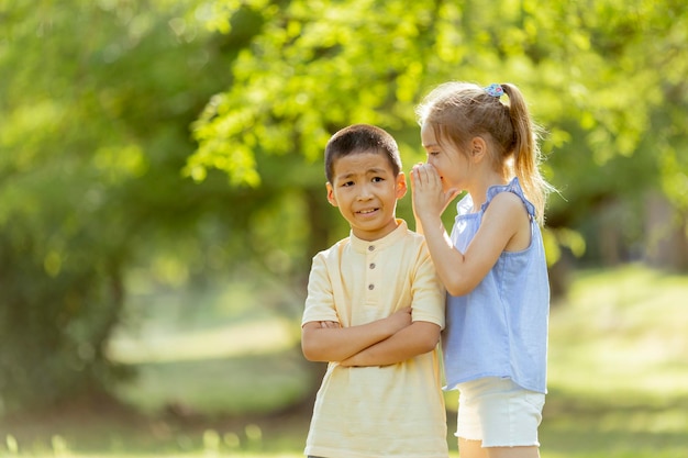 公園でアジアの男の子に秘密を告げる白人の女の子