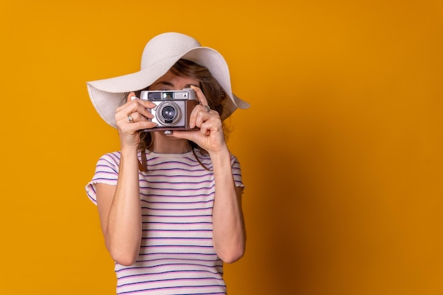 夏休みの黄色の背景を楽しんで写真を撮る帽子と観光コンセプトの白人の女の子