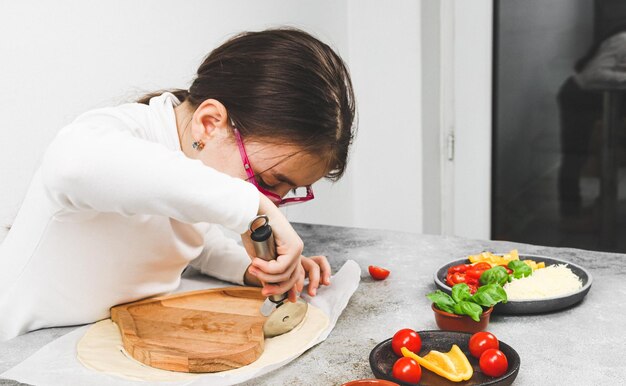 Caucasian girl in a white turtleneck cuts dough on a wooden plate with a metal scabbard