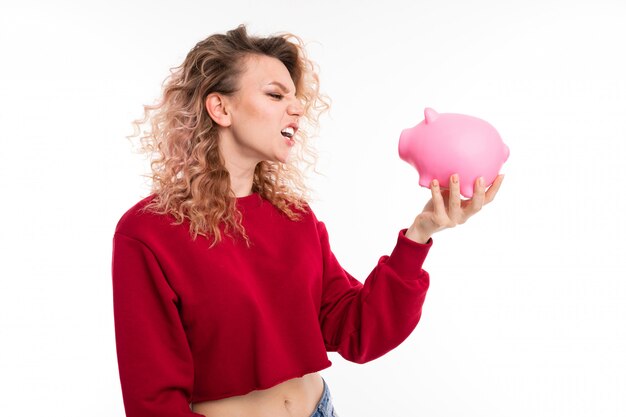 Caucasian girl with curly fair hair holds a pink pig moneybox, portrait isolated