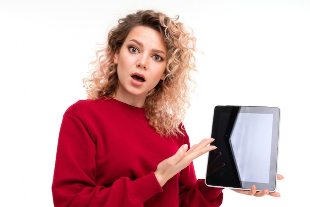 Caucasian girl with curly fair hair holds a tablet and is surprised