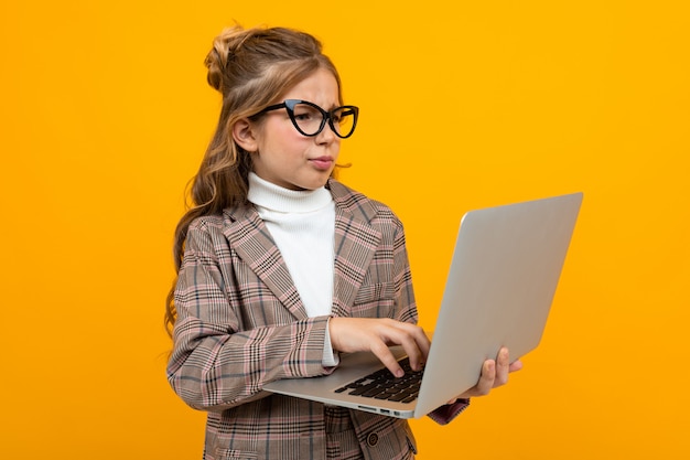 Caucasian girl with glasses in a business suit with a laptop in hands on yellow