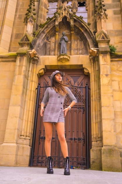 Ragazza caucasica con abito grigio e un berretto accanto a una cattedrale in una posa fotografica