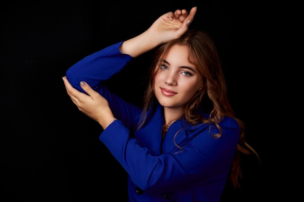 Caucasian girl with long hair in a blue dress posing on a black background