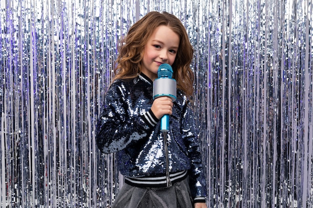 Photo caucasian girl with a microphone on the wall of tinsel