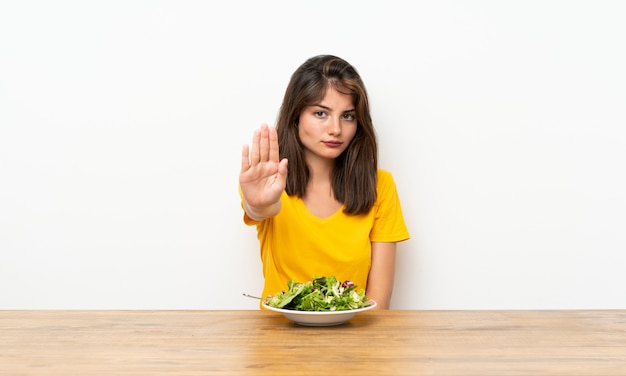 Ragazza caucasica con l'insalata che fa gesto di arresto con la sua mano