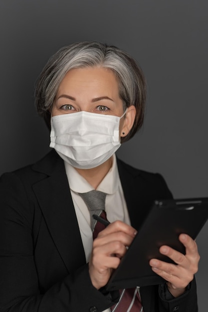 Caucasian grey haired businesswoman in protective mask work using digital tablet gadget looking at c...