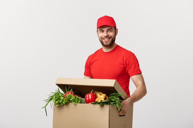 Caucasian grocery delivery courier man in red uniform with grocery box with fresh fruit